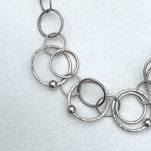 A close up detail of the necklace showing the mix of hammered and smooth circular links, accented with delicate silver beads.