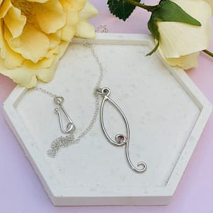 A stylized, elongated teardrop with a pink tourmaline nestled a small spiral. Handcrafted in Sterling Silver.