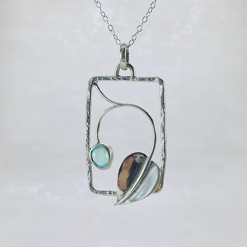 Set with in a lightly textured Sterling Silver rectangular frame, a large leaf sits at the bottom with a curling vine branching out to a pale blue Chalcedony ovel set gemstone. The pendant hangs on a delicate Sterling Silver chain with a handmade S Clasp